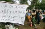 A Hmong hilltribe family with belongings walks past a banner erected at Ban Huan Nam Khao village in Petchabun province, northeastern Thailand, after being forced to leave their homes Tuesday, July 5, 2005.