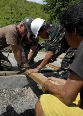 Seabees with Amphibious Construction Battalion (ACB) 1 stabilize a two-by-four while a member from the Philippine Army 54th Engineering Brigade saws.