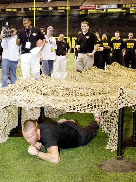 Dax Thomas, an ROTC cadet with the University of Oklahoma , shows U.S. Army All American Bowl media competitors the mechanics of the low crawl during a media challenge contest at the Alamodome in San Antonio.The three-event contest pitted media repres