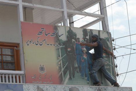 An Indian Kashmiri protestor climbs up a wall to tear down a billboard of a pro-India party during a demonstration in Srinagar on June 27, 2008.