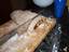 A 'loaf' of raw cinnamon roll dough being cut into individual rolls prior to being baked.