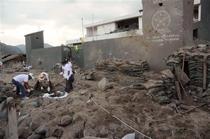 Men inspect the body of a police officer after the police station was attacked with a car bomb and mortars in Toribio, Colombia, Saturday July 9, 2011.