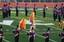 Two color guard members dressed in togas spin flags with fire designs in the middle of the DVC football field.