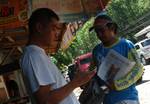 A man is texting on his cellphone as a newspaper boy approaches; Philippines