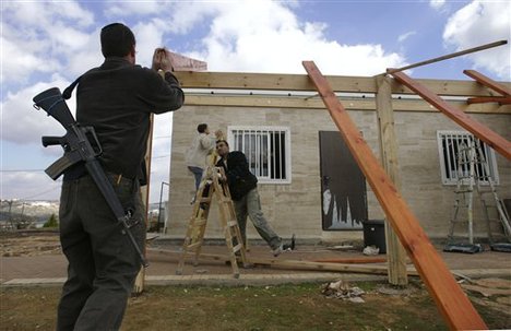 File - An armed Jewish settler, left, and Palestinian workers builds an awning at the synagogue of the unauthorized West Bank outpost of Bruchin, Monday, Jan. 7, 2008.