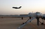 A C-17 Globemaster III takes off from Balad Air Base, Iraq as a U.S. Air Force MQ-1L Predator Unmanned Aerial Vehicle (UAV) waits to be launched.