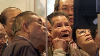 Elderly investers crowd around a share price monitor at a brokerage in Hong Kong