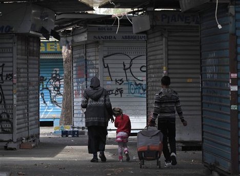 A woman and children walk past closed market kiosks, in Rome, Monday, April 2, 2012. The number of people looking for work in the 17 countries that use the euro hit its highest level since the currency was introduced back in 1999