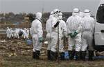 Japanese police officers wearing white suits to protect them from radiation stand by a victim being cleaned as other officers carry another body in the background while searching for missing people in Minami Soma, Fukushima Prefecture, northeastern Japan Friday, April 8, 2011. Hundreds of Japanese police and soldiers have been mobilized in a major search operation inside the deserted evacuation zone within the 20 kilometer radius from the Fukushima Dai-ichi nuclear reactors.