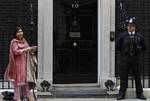 Under the watchful eye of a British police officer, right, Baroness Sayeeda Warsi, left, the Conservative Party's co-chairman and newly appointed minister without portfolio removes her coat so she can pose for the photographers per their request, as she leaves following the first cabinet meeting at British Prime Minister David Cameron official residence at 10 Downing Street in central London, Thursday May 13, 2010.