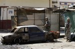 Lebanese army soldiers walk past a car damaged during fighting in the northern port city of Tripoli, Lebanon, Sunday, June 3, 2012.