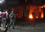 In this Monday, June 18, 2012 photo, Lebanese army soldiers and civilians look on as a fire burns at a Lebanese army checkpoint at the main entrance of the Ein el-Hilweh Palestinian refugee camp in Sidon, Lebanon. Residents of the camp are protesting after clashes broke out Monday in the Nahr el-Bared camp in the north of Lebanon.