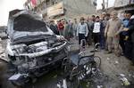 People inspect a destroyed car and a wheelchair at the scene of a car bomb attack Baghdad, Iraq, Thursday, Jan. 27, 2011. A car bomb ripped through a funeral tent in a mainly Shiite area of Baghdad on Thursday, killing and wounding scores of people and prompting scuffles between police and Iraqis angry about security failures.