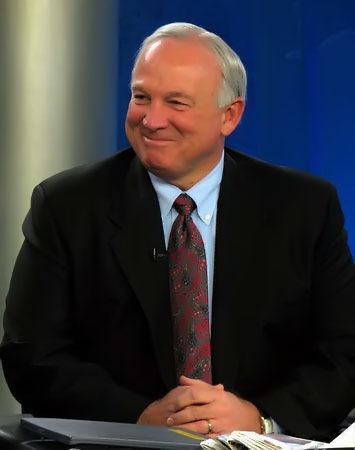 Waist high portrait of man in his sixties, smiling in a black suit