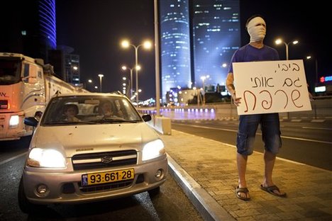 An Israeli man covers his face with a bandage as others, not seen, block a highway in Tel Aviv on Sunday, July 15, 2012, during a protest against the economic policies of Israel's government and to show solidarity with Moshe Silman, an Israeli protester who set himself on fire on Saturday during a protest.