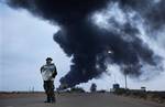 A pro-Gadhafi fighter holds a poster of Libyan Leader Moammar Gadhafi as black plume of smoke rises from the burning oil refinery as they are pictured during a government-organized visit for foreign media in Ras Lanouf, 380 miles (615 kilometers) southeast of the capital Tripoli, in Libya Saturday, March 12, 2011. The world moved a step closer to a decision on imposing a no-fly zone over Libya but Moammar Gadhafi was swiftly advancing Saturday on the poorly equipped and loosely organized rebels