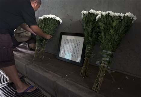 A Chinese man places flowers next to a frame with the names of flood's victim under a railway bridge, where a motorist drowned a week ago in Beijing, China Saturday, July 28, 2012. A small group of people laid down white chrysanthemums or lit candles Saturday to pay tribute to those who died in the storm that ravaged Beijing one week ago, killing at least 77.