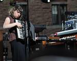 Conlee playing accordion, with organs and other instruments nearby. The band's songs range from upbeat pop to instrumentally lush ballads, and often employ instruments like the accordion, Hammond organ, Wurlitzer organ, and upright bass.