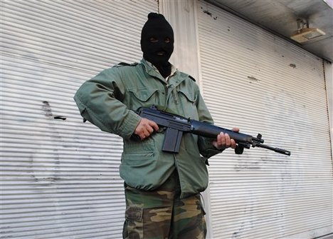 File - A Syrian army defector stand guards in front of closed shops at the mountain resort town of Zabadani, Syria, near the Lebanese border, on Friday Jan. 20, 2012.