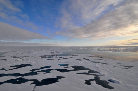 Parallel cloud bands converge at the horizon over a landscape of ice floes, melt pools, and a polynya to the right.