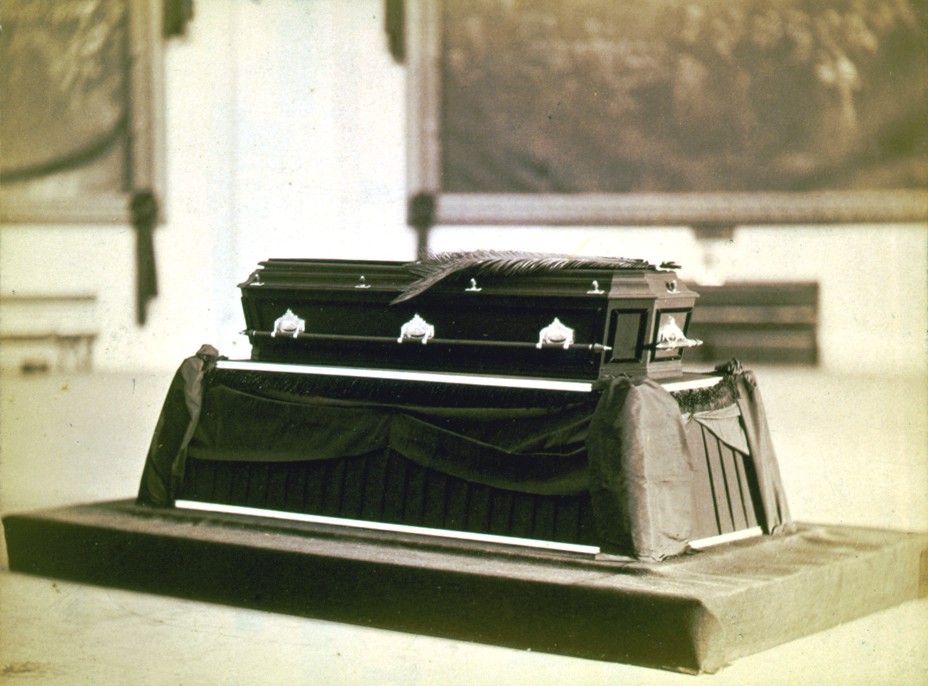 A casket sits on a bier in this black and white photo