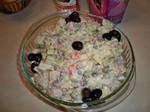 A homemade variant of the Russian Salad containing potatoes, peas, cabbage, sweet gherkins, capers, ham, carrots, olive oil, wine vinegar, dijon mustard and sour cream, garnished with black olives.