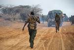 SOMALIA, Kismayo: In a handout photograph taken 02 October by the African Union-United Nations Information Support Team and released 03 October, a fighter of the Ras Kimboni Brigade, a Somali government-allied militia walks along a road as a soldier from the Kenyan Contingent of the African Union Mission in Somalia (AMISOM) runs in the other direction during an advance on the Somali port city of Kismayo. Kenyan AMISOM troops moved into and through Kismayo, the hitherto last major urban stronghol