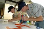 Mineman 1st Class Ammie Faucett and Electrician's Mate 3rd Class Levi Martin of High Speed Vessel (HSV) 2 Swift paint a sign during a community relations project at the Hogar de Ninos San Ramon orphanage.