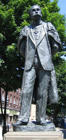 photograph of modern statue of Edwardian male figure with a large moustache in academic gown and wearing badge of the Order of Merit