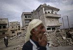 In this Wednesday, Dec. 12, 2012 photo, an elderly Syrian man smokes a cigarette while standing next to a residential building destroyed in a government airstrike, in Maaret Misreen, near Idlib, Syria.