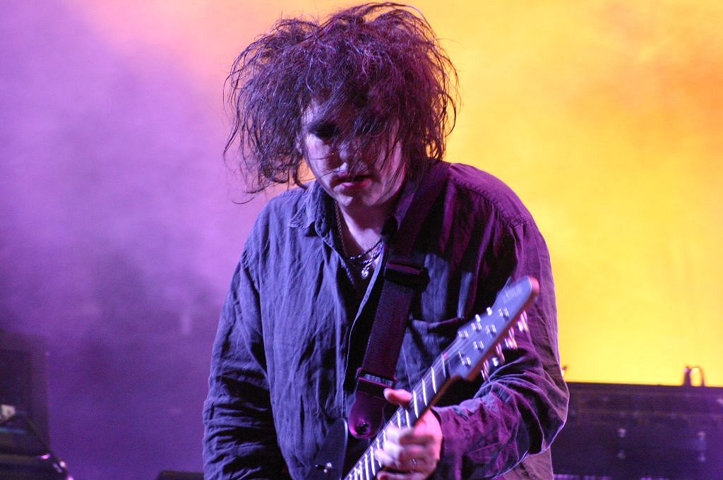 Head and shoulders shot of man, with wild, tangled hair and lipstick on,  playing in a stage spotlight.