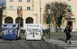 A woman walks past a trash bin defaced with a graffiti reading "Electoral boot. Vote here " in Rome, Monday, Feb. 18, 2013.