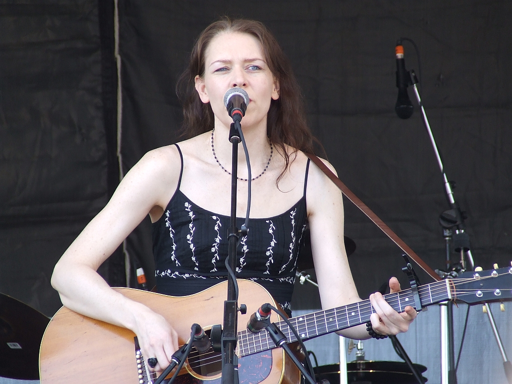 Welch singing and playing guitar on stage, wearing a black dress.