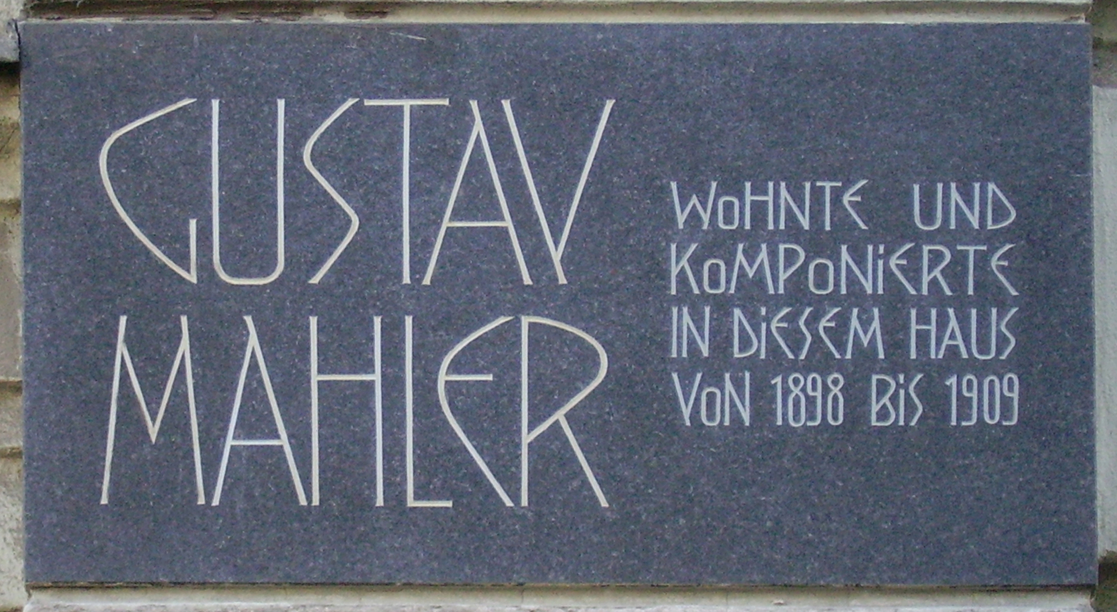  A dark plaque with white lettering in which the composer's name is shown in extra large characters on the left, the main message in smaller characters on the right