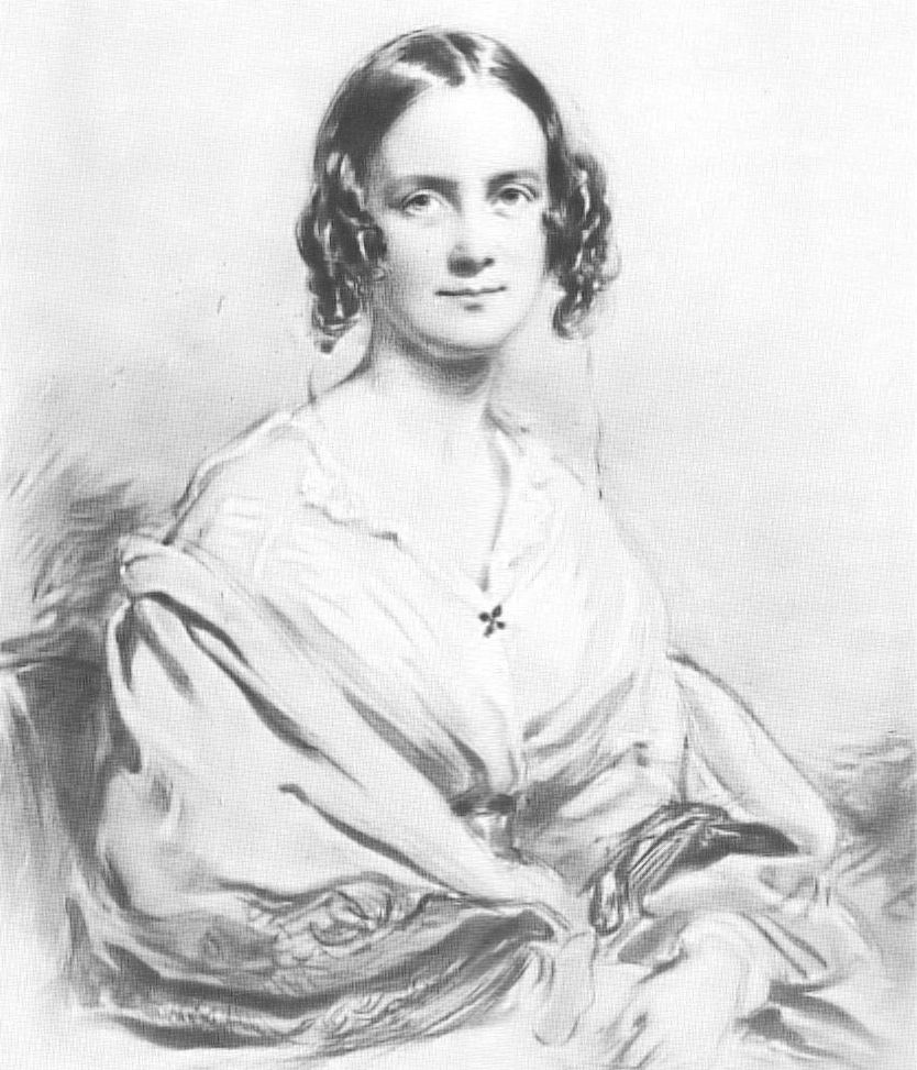 Three quarter length portrait of woman aged about 30, with dark hair in centre parting straight on top, then falling in curls on each side. She smiles pleasantly and is wearing an open necked blouse with a large shawl pulled over her arms