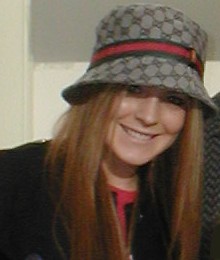 A red-haired Caucasian female wearing a black coat and a hat