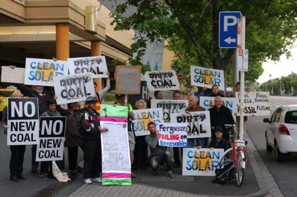 Protesters line up with 'no coal' and 'clean solar' placards outside hotel