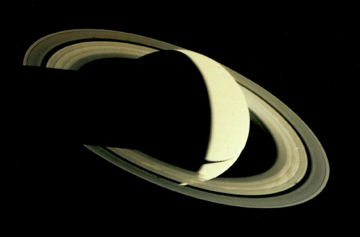 View of Saturn lit from the right. Saturn's globe casts its shadow over the rings to the left. Part of the lower hemisphere can be seen through the rings. Some of the spoke-like ring features are visible as bright patches.