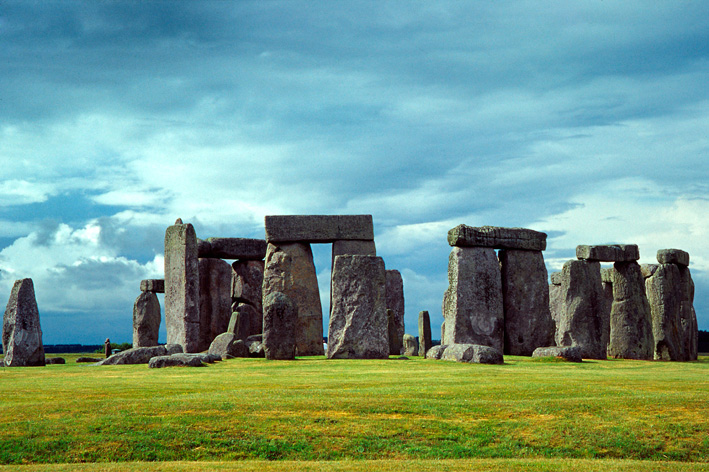 Sun shining through row of upright standing stones with other stones horizontally on the top.