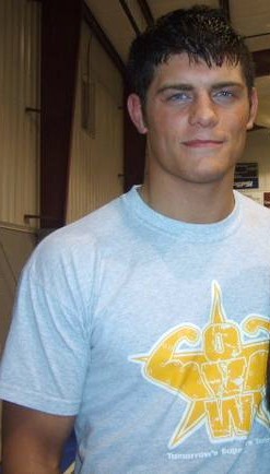 A close-up of a young Caucasian male with black hair. He is wearing a light-colored t-shirt with the yellow logo of the Ohio Valley Wrestling promotion upon it.