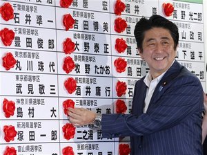 Japanese Prime Minister Shinzo Abe smiles as he places a red rosette on the name of his Liberal Democratic Party's winning candidate during ballot counting for the upper house elections at the party headquarters in Tokyo Sunday, July 21, 2013.