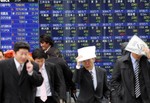 Pedestrians cover their heads to protect from the rain in front of the electronic stock board of a securities firm in Tokyo Tuesday, Feb. 24, 2009. Japanese shares tumbled early Tuesday after a brutal session on Wall Street overnight, but the sell-off eased as the government signaled it may move to prop up stock prices. The benchmark Nikkei 225 stock average lost 1.5 percent, or 107.6 points, to 7,2