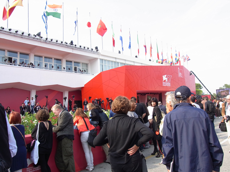 A line outside the entrance to the 2010 Venice International Film Festival with flags of several countries waving above the door