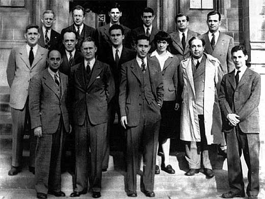 A group of people in suits standing in three rows on the steps in front of a stone building.