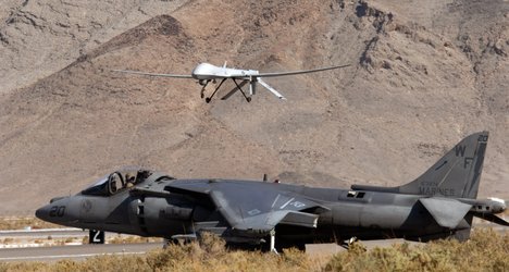 File - A U.S. Marine Corps AV-8B Harrier waits as a MQ-1 Predator lands Nov. 7, 2008, at Creech Air Force Base, Nev.