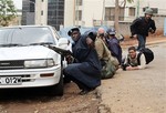 Kenyan security personnel and journalists duck behind a vehicle as heavy gunfire erupts from the Westgate Mall in Nairobi Kenya Monday Sept. 23 2013.