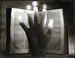 Hand with candle-lit finger tips over an open book