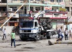 Citizens inspect the site of a car bomb attack while security forces prepare to tow away a destroyed car in Baghdad, Iraq, Monday, Sept. 30, 2013.