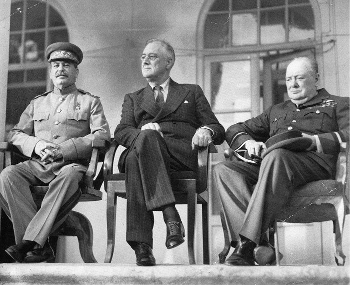 Three men, Stalin, Roosevelt and Churchill, sitting together elbow to elbow