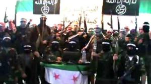 this picture shows a gathering of al qaeda forces, standing behind a syrian flag, with two al qeada flags behind them.